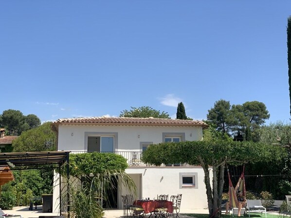 A two-story house with a tiled roof, a balcony, and a garden area with a table and chairs.