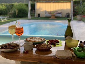 A dining table with food and drinks, a bottle of wine, and a pool in the background.