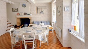 Zona pranzo con pavimento a scacchi, arredi bianchi, camino e finestra con tende.