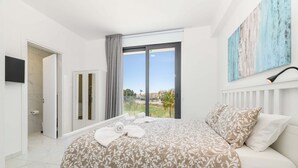 Une chambre avec un grand lit, une vue à travers une porte-fenêtre coulissante, un tableau au mur et un téléviseur fixé au mur.