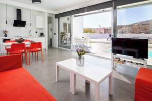 A modern living space with a kitchen, dining area, and a balcony with a TV. - Villa Paradiso Tria - Two Bedroom Villa, Sleeps 4 (Malevizi)