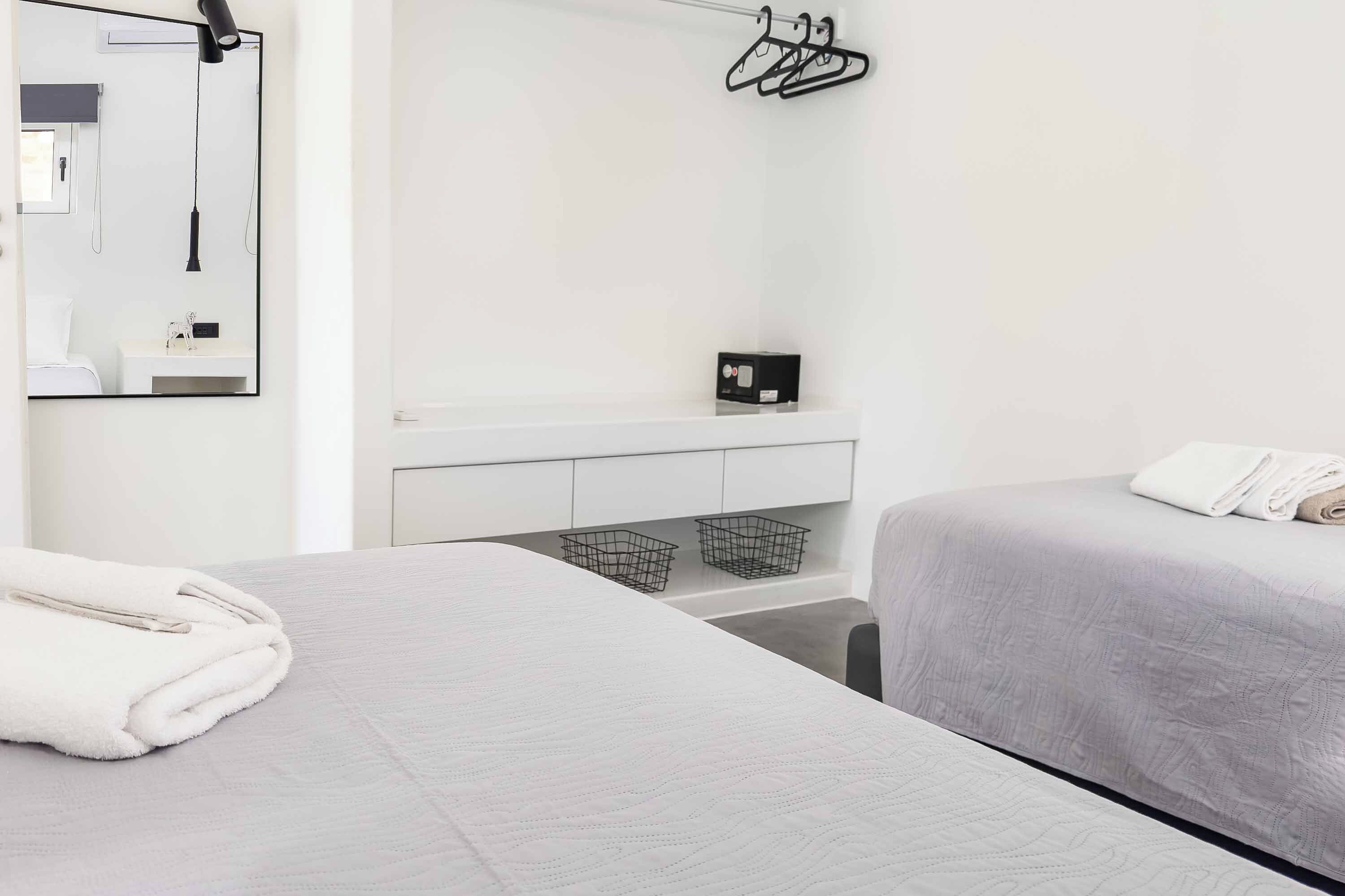 A hotel room with a bed, a bedside table, a mirror, a hanging light, a towel, and a small shelf with a box.