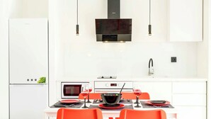 Una cocina moderna con armarios blancos, una campana extractora negra y un comedor con sillas anaranjadas y una mesa blanca.
