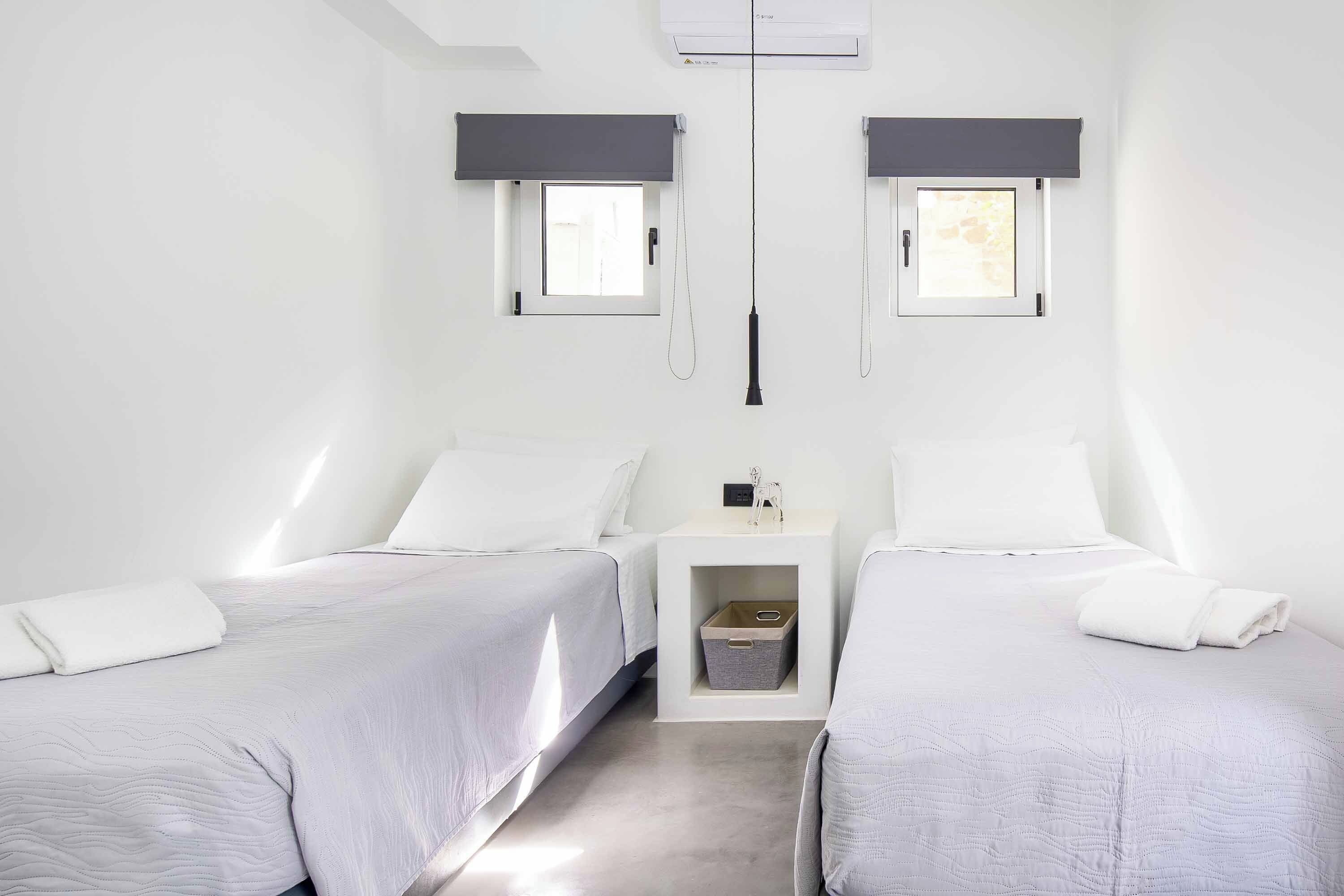 Un dormitorio minimalista con dos camas, una mesita de noche pequeña y un equipo de aire acondicionado de pared.