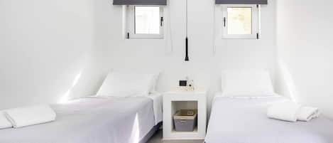 Un dormitorio minimalista con dos camas, una mesita de noche pequeña y un equipo de aire acondicionado de pared.
