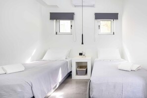A minimalist bedroom with two beds, a small bedside table, and a wall-mounted air conditioning unit. - Villa Paradiso Tria - Two Bedroom Villa, Sleeps 4 (Malevizi)