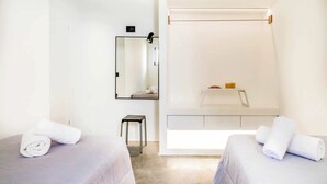 Habitación de hotel con dos camas, un taburete pequeño, un espejo y una ventana con cortina.