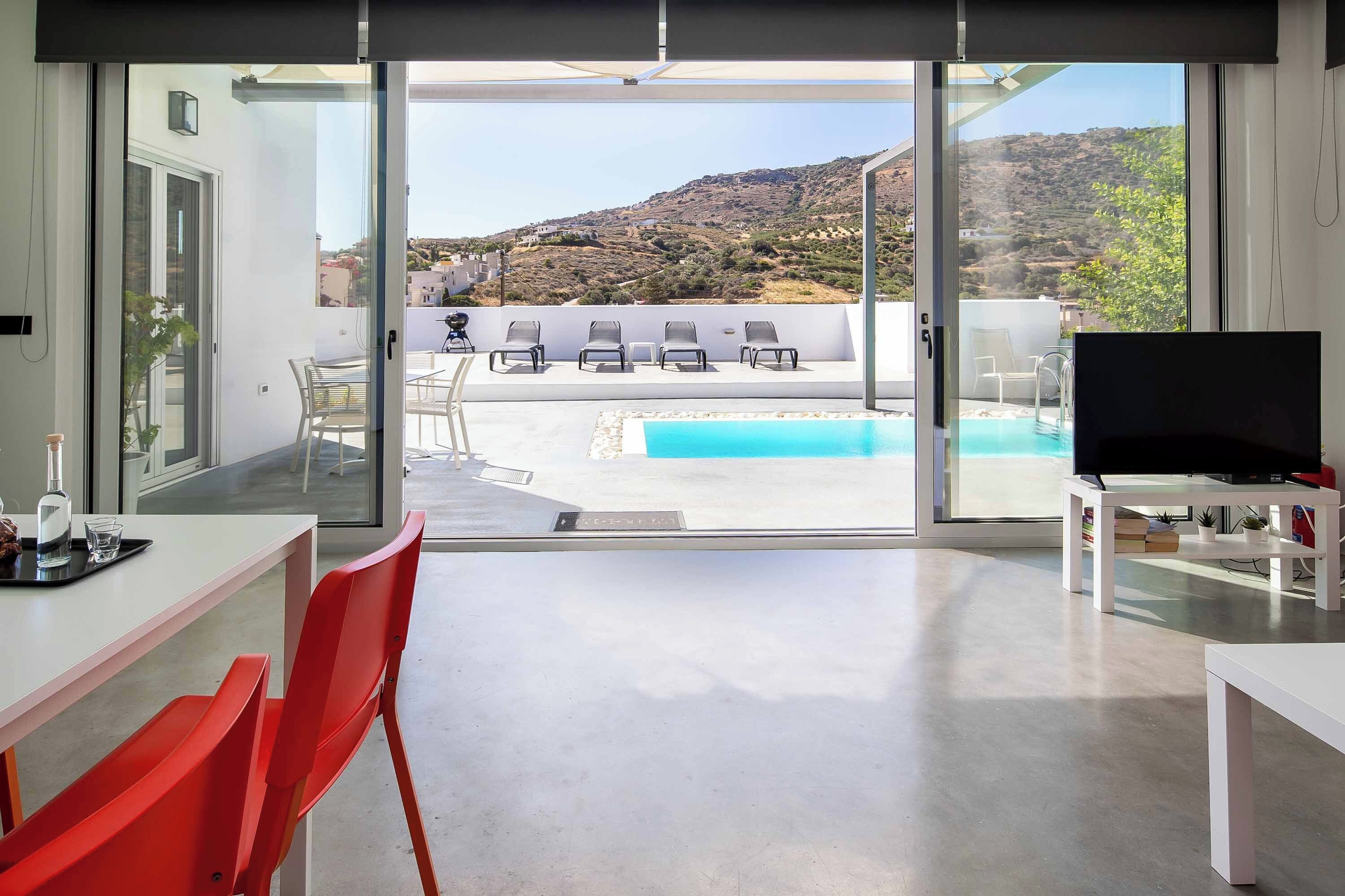 Una sala de estar moderna con un gran ventanal corredero que da a una zona de piscina y vistas de un paisaje montañoso.