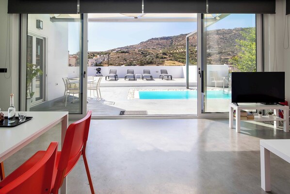 A modern living room with a large sliding glass door leading to a pool area with a view of a hilly landscape.