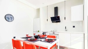 Una cocina moderna con armarios blancos, una campana extractora negra y un comedor con mesa blanca y sillas naranjas.