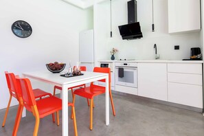 A modern kitchen with white cabinets, a black microwave, and a dining area with a white table and red chairs. - Villa Paradiso Tria - Two Bedroom Villa, Sleeps 4 (Malevizi)