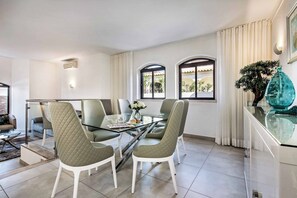 A modern dining area with a glass table and chairs, a view of the outdoors through windows, and a decorative vase on a cabinet. - Villa Marquesa - Four Bedroom Villa, Sleeps 8 (Algarve)