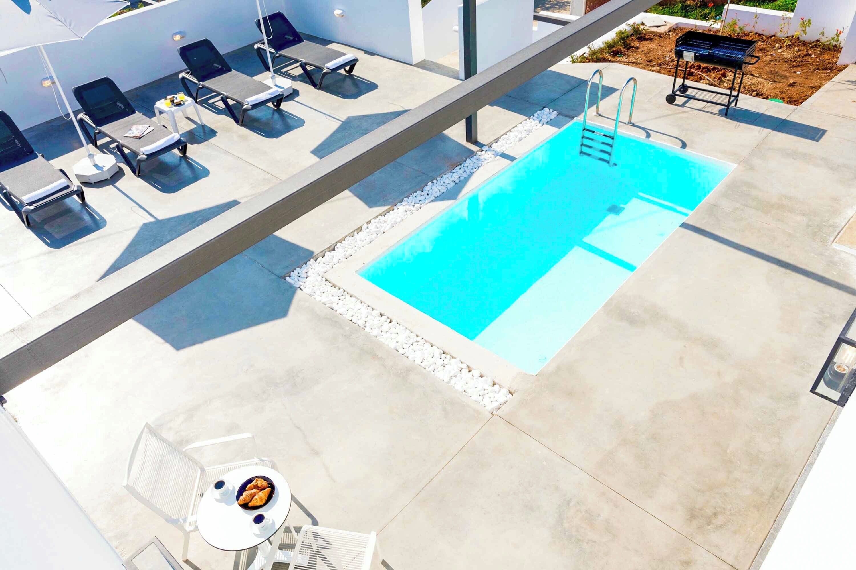 A rooftop pool area with lounge chairs, a barbecue grill, and a table with food.