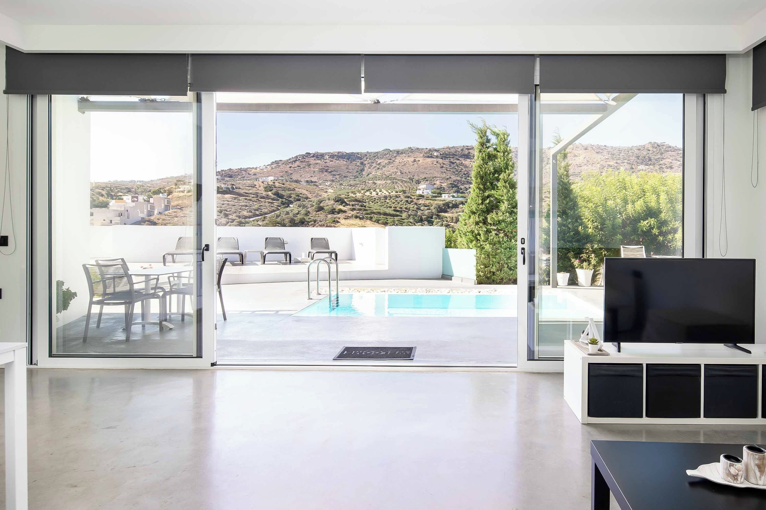 Una sala de estar moderna con piscina, puertas correderas de vidrio y vistas a un paisaje montañoso.
