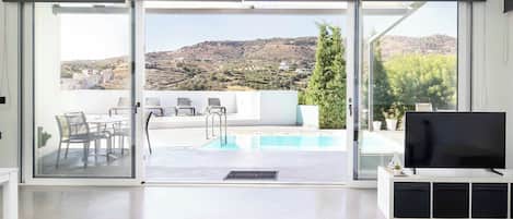 Una sala de estar moderna con piscina, puertas correderas de vidrio y vistas a un paisaje montañoso.
