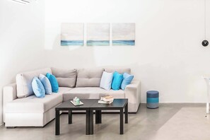A modern living room with a beige sectional sofa, a black coffee table, and a blue accent stool. There are three abstract paintings on the wall above the sofa. - Villa Paradiso Tessera (Malevizi)
