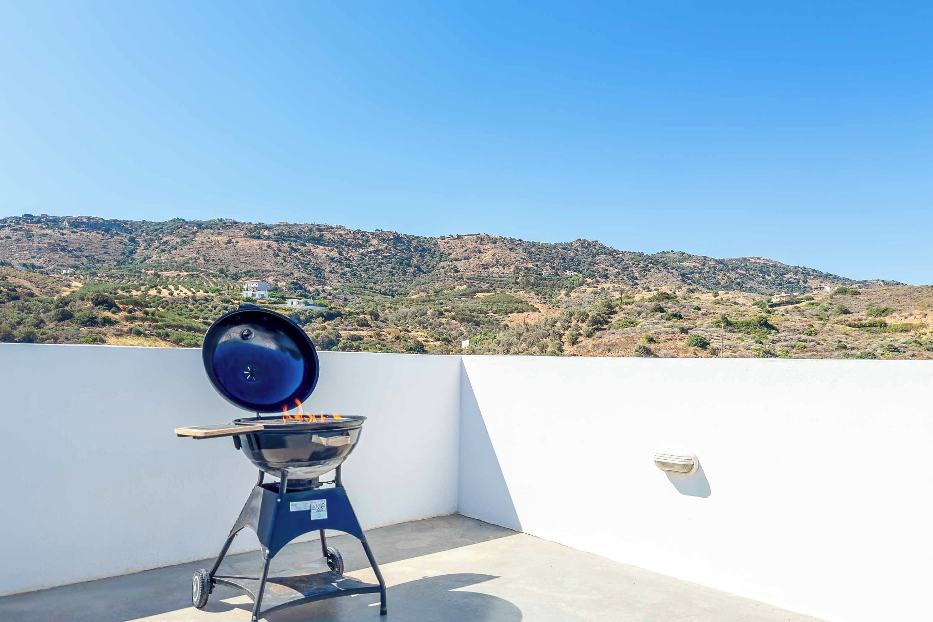 A barbecue grill on a rooftop with a view of a hilly landscape.