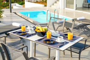 A breakfast setup with a pool view, including a table with breakfast items, chairs, and a poolside setting.