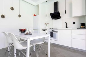 A modern kitchen with white cabinetry, a dining table with chairs, and a built-in oven. - Villa Paradiso Tessera (Malevizi)