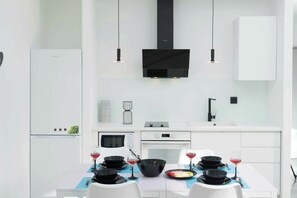 Una cocina moderna con armarios blancos, extractor de aire negro, horno empotrado y una mesa de comedor con utensilios de cocina negros y copas de vino.