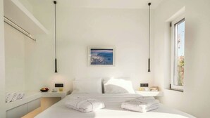 Ein modernes Hotelzimmer mit einem großen Bett, weißen Leinen, einem Gemälde über dem Bett und einem Fenster an der Seite.