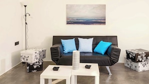 Ein modernes Wohnzimmer mit einer schwarzen Ledersofa, zwei blauen Kissen, einem weißen Couchtisch und passenden Beistelltischen mit floralem Muster.