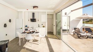Eine moderne Küche mit weißen Schränken, ein Essbereich mit weißen Stühlen und eine Glastür, die auf einen Balkon mit Tisch und Stühlen führt.