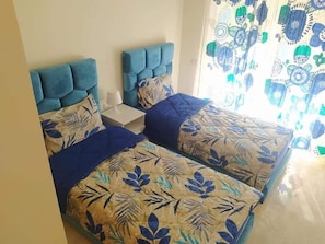 Quarto com duas camas, cada uma com cabeceira azul e roupa de cama florida.