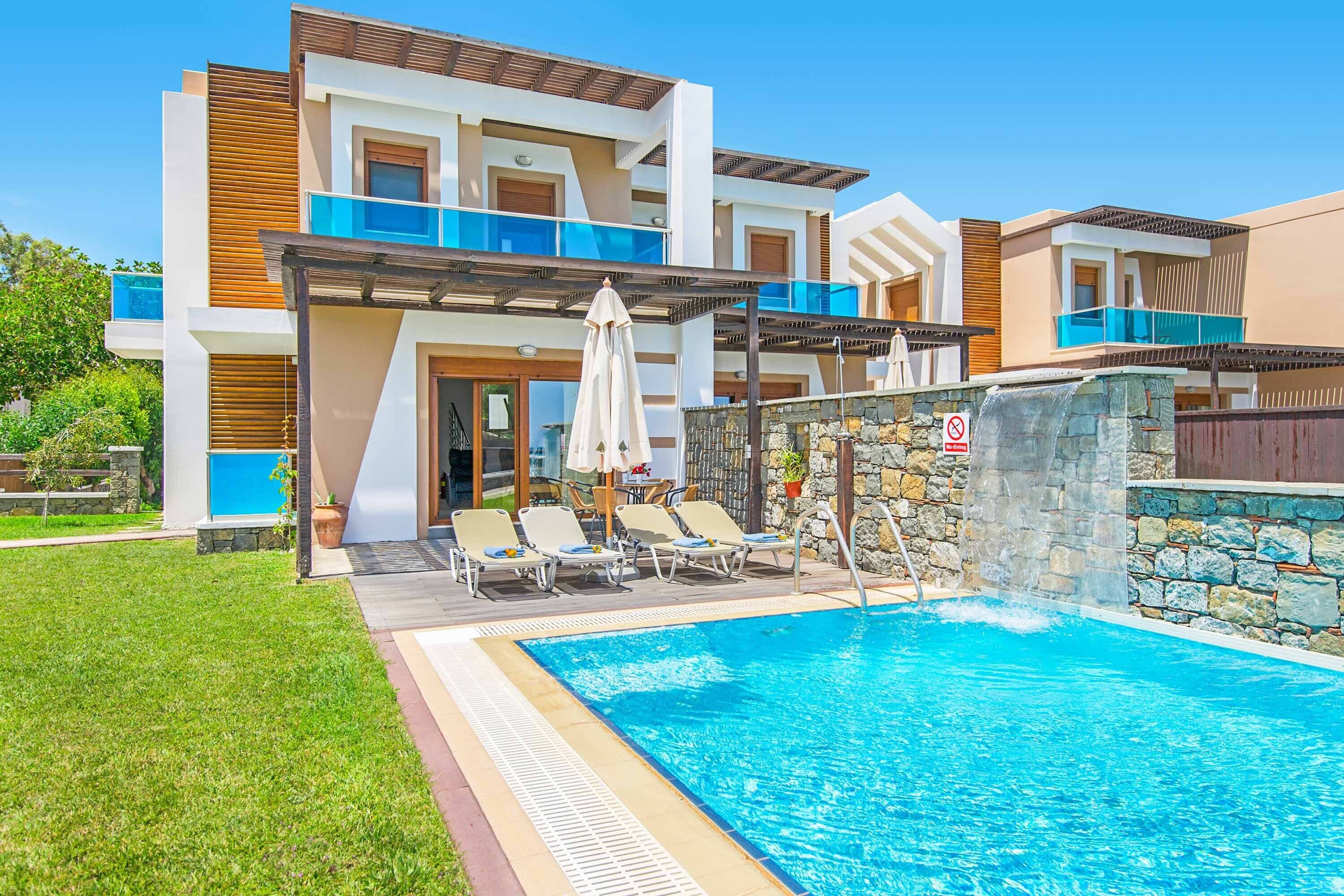 Un edificio moderno de varios pisos con piscina, mobiliario exterior y un muro de piedra.