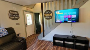 Una sala de estar con un sofá de cuero, un televisor montado que muestra servicios de streaming, y un letrero de un negocio local.