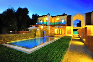 Une maison moderne à deux étages, dotée d’une piscine, d’un espace extérieur aménagé et d’un patio bien éclairé.