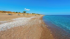 Ein Strand mit Kieselsteinen, blauem Himmel und einigen Sonnenschirmen.