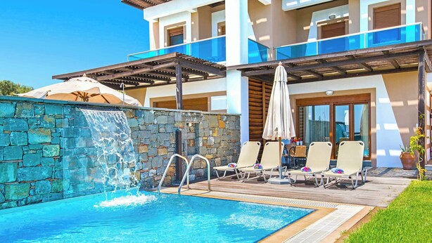 Ein Schwimmbecken mit Wasserfall, Liegestühlen und einer überdachten Terrasse.