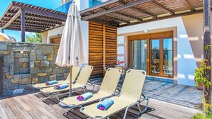 Eine Terrasse mit vier Liegestühlen, einer Holzpergola und einer Steinmauer.