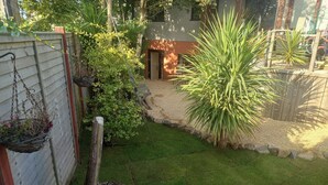 Een verzorgde tuin met een houten omheining, verschillende planten en een grindpad dat naar een gebouw leidt.