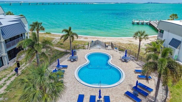 A pool with lounge chairs, a beach, and a pier.