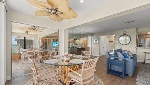 A spacious living area with a dining table, chairs, a blue sofa, and a ceiling fan.