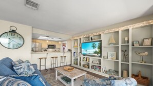 A living room with a sofa, coffee table, TV, and a kitchen in the background.