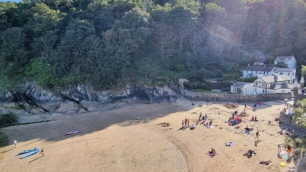 Una playa con gente, un muro de piedra y un edificio de fachada blanca.