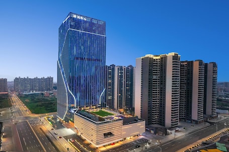 A modern high-rise building with a unique angular design, surrounded by other high-rise buildings.. Wyndham Shanwei Haifeng