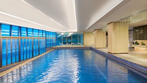 Una piscina interior con paredes de vidrio transparente, una zona de recepción y vistas al cielo.