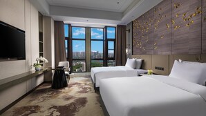 Habitación de hotel con dos camas, televisión, escritorio y un amplio ventanal con vista a la ciudad.