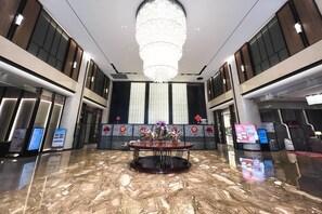 A lobby with a marble floor, a round table with flowers, a chandelier, and a wall with vertical windows and decorative panels. - Wyndham Shanwei Haifeng (Shanwei)