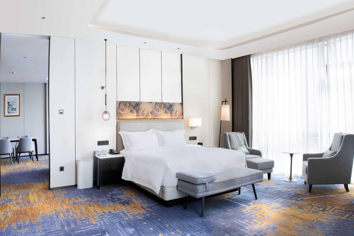 A hotel room with a large bed, two armchairs, a desk, and a view of the city.