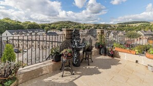 A rooftop terrace with potted plants, a stone sculpture, and a view of a town with houses and hills in the background. - 3 bedroom accommodation in Buxton (Buxton)