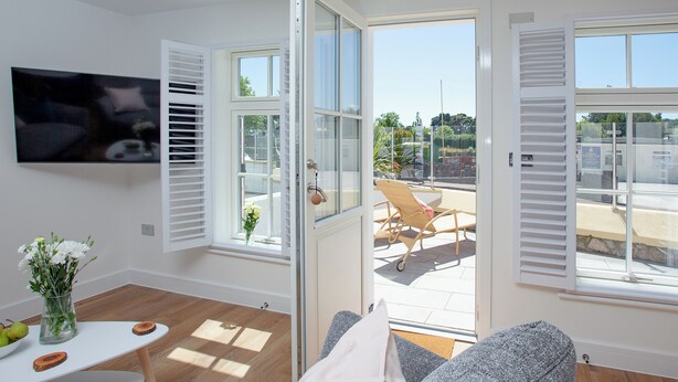 Ein helles Wohnzimmer mit Fernseher, einer Glastür, die nach draußen führt, und Blick auf eine Terrasse.