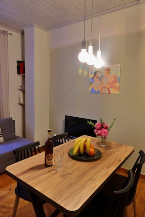 Un coin repas avec une table en bois, des chaises, une bouteille de vin, un verre et un panier de fruits.