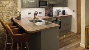 Eine moderne Küche mit einer zentralen Kochinsel, grauen Schränken, einem eingebauten Backofen und einer Wand mit Natursteinverkleidung.