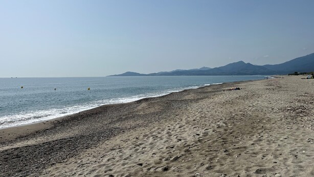 Ein Strand mit Kiesküste, ruhigem Meer und fernen Bergen.