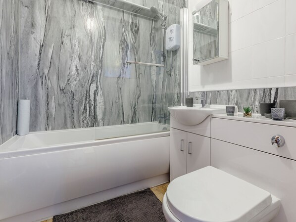 A modern bathroom with a marble wall, a bathtub, a toilet, and a sink with a mirror above.
